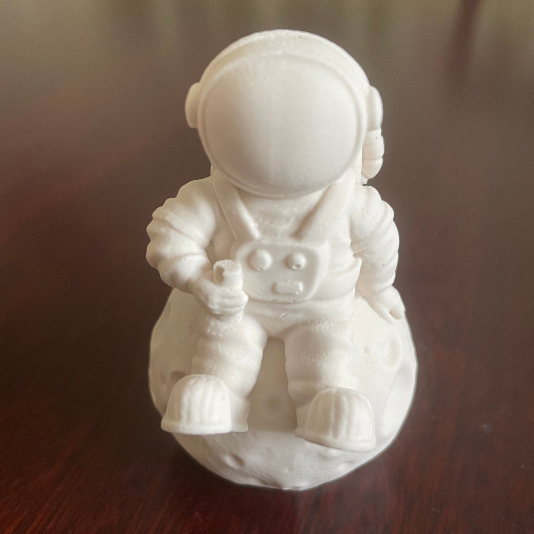 image shows a spaceman sat on a moon in a white colour 