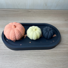 Load image into Gallery viewer, image shows a black oval tray with a copper coloured foil running length ways sat on top of the tray is 3 jesmonite pumpkins in black orange and yellow. 
