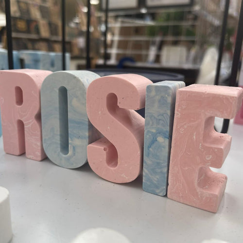Jesmonite letters spelling the name Rosie, in pink and white and blue and white. 